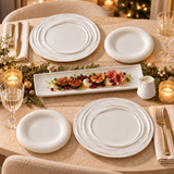 Table de fête avec grandes assiettes blanches à relief ondulé, petites assiettes rondes, plat rectangulaire et saucière blancs.