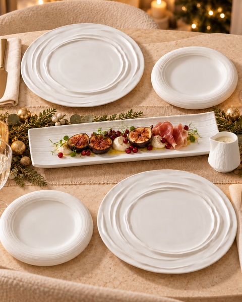 Table de fête avec grandes assiettes blanches à relief ondulé, petites assiettes rondes, plat rectangulaire et saucière blancs.