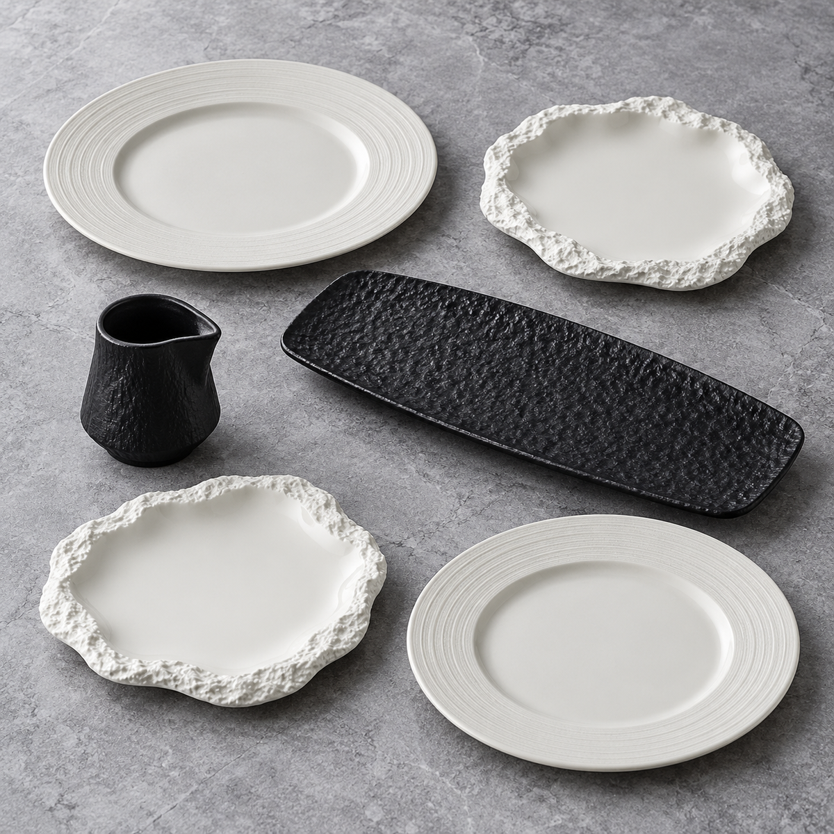 Coffret Minéral d’hiver : quatre assiettes blanches aux bords striés ou rocheux, un plat rectangulaire et une saucière noirs.