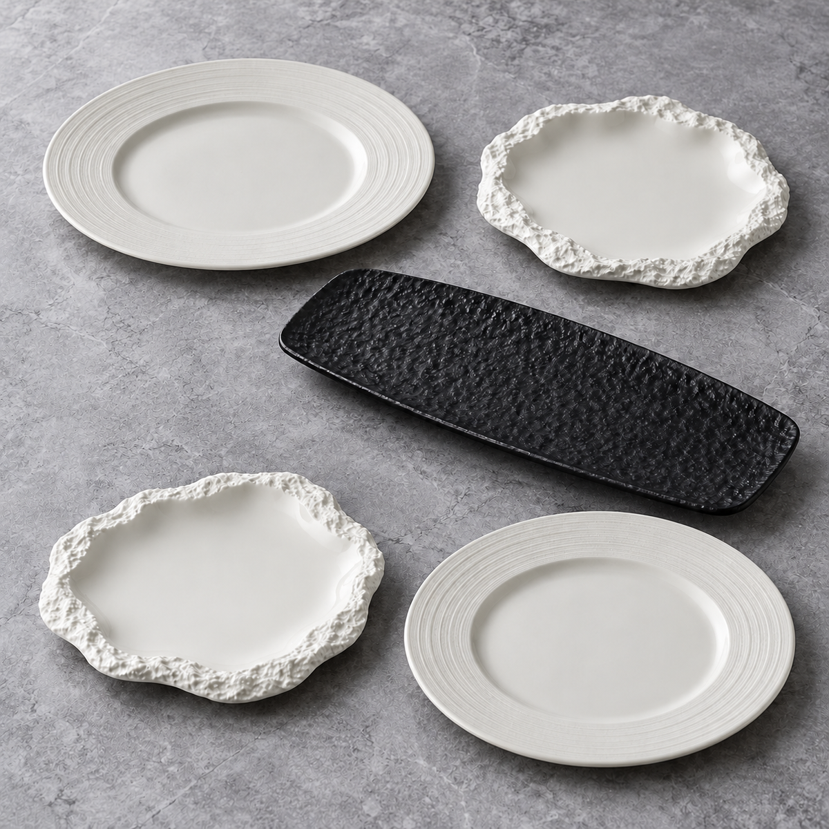 Quatre assiettes blanches, deux à bord strié et deux à bord rocheux, avec un plat rectangulaire noir sur fond gris.