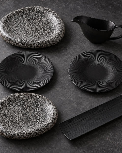Coffret Nuit de fête : deux assiettes mouchetées, deux assiettes noires striées, un plat rectangulaire et une saucière noirs.
